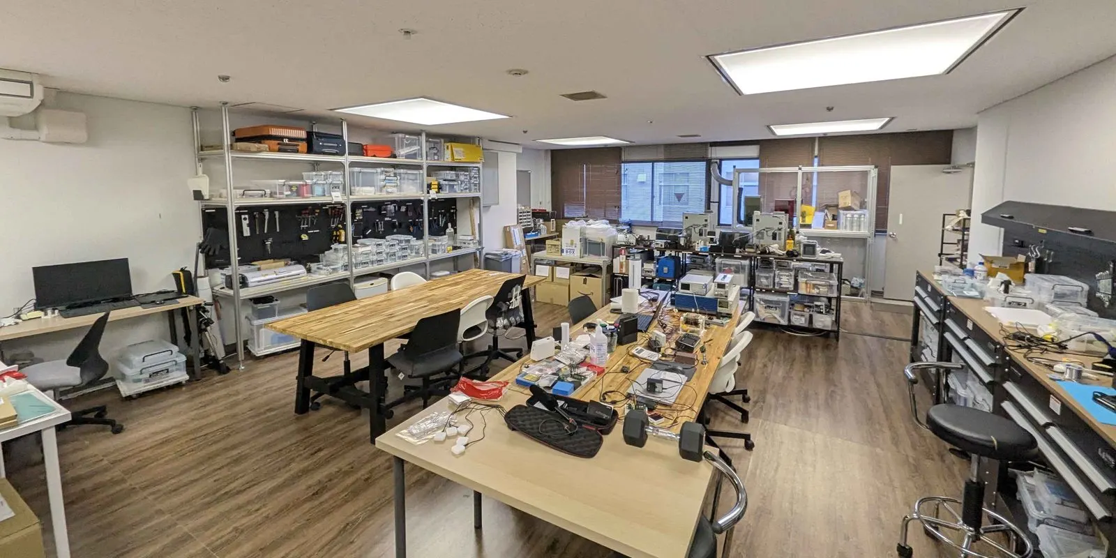 The Osaka Heat Cool lab: wooden workbenches with devices under construction and tools, and shelves of parts and measuring instruments at the back