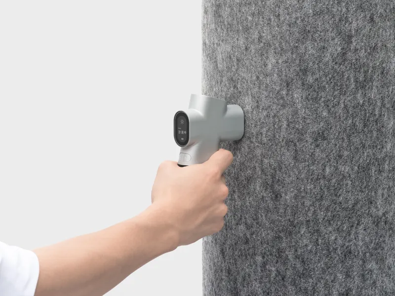 A hand pressing ThermoFeel p against gray felt fabric, with the display reading measuring